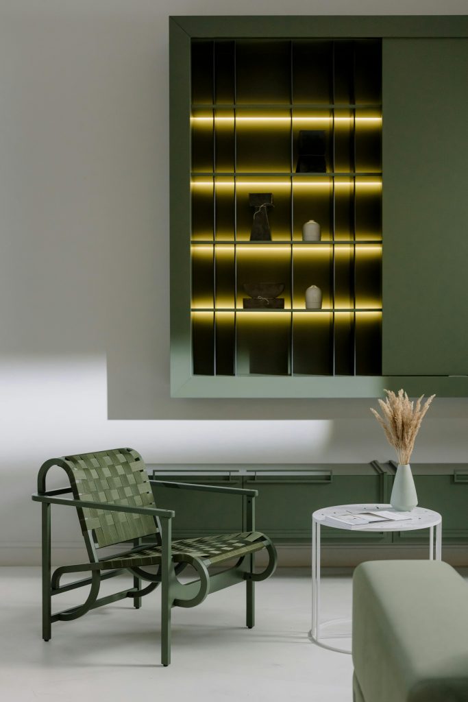 Best Furniture Design Materials for Sustainable Interiors 2 Stylish living room with a green armchair, illuminated shelves, and a minimalistic table with dried flowers.