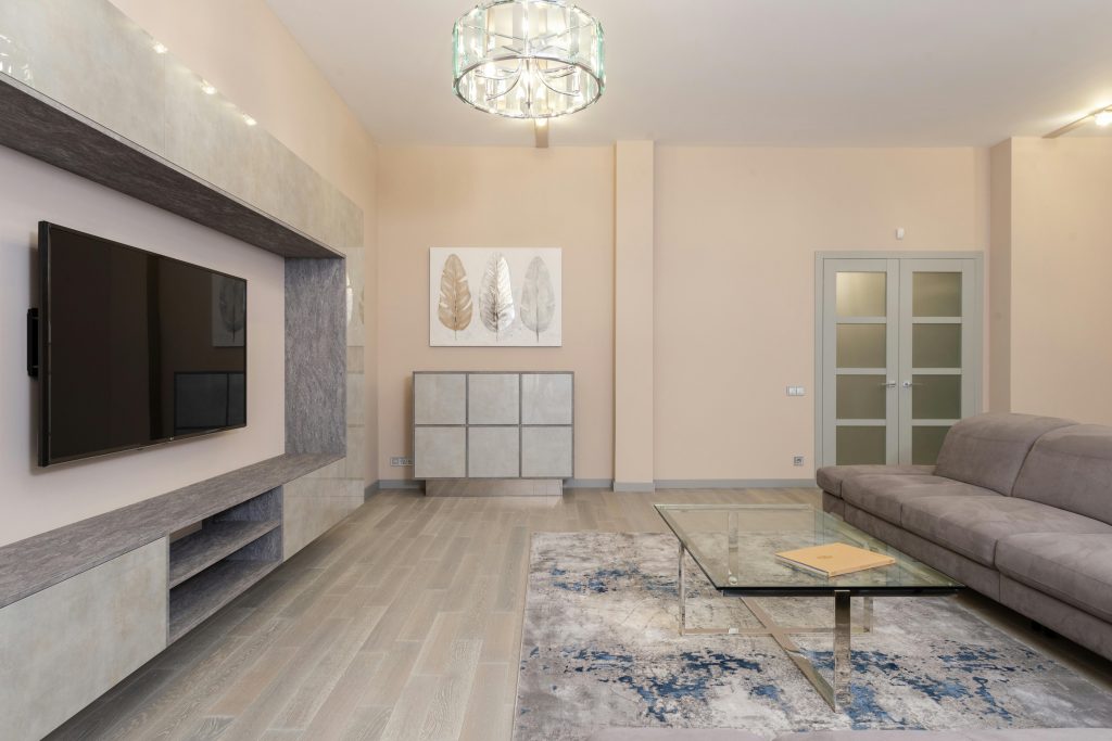 Best Furniture Design Materials for Sustainable Interiors 4 A spacious living room featuring modern decor with a gray sofa, glass table, and large TV.